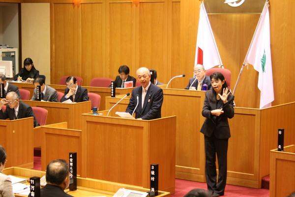 手話通訳者が市長の横に立って、市長の答弁を手話で通訳している様子の写真